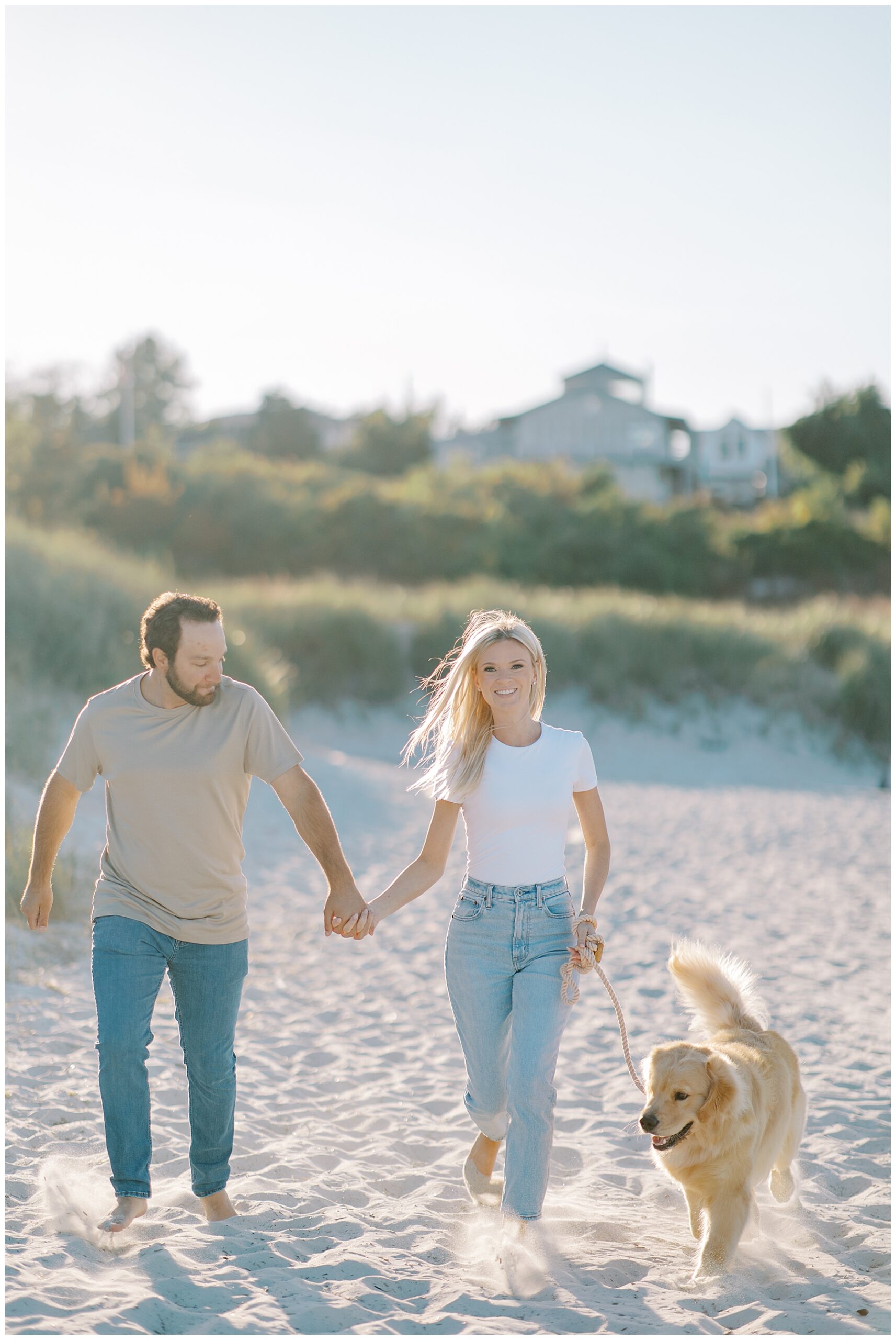 couple holding hands run across beach with their dog