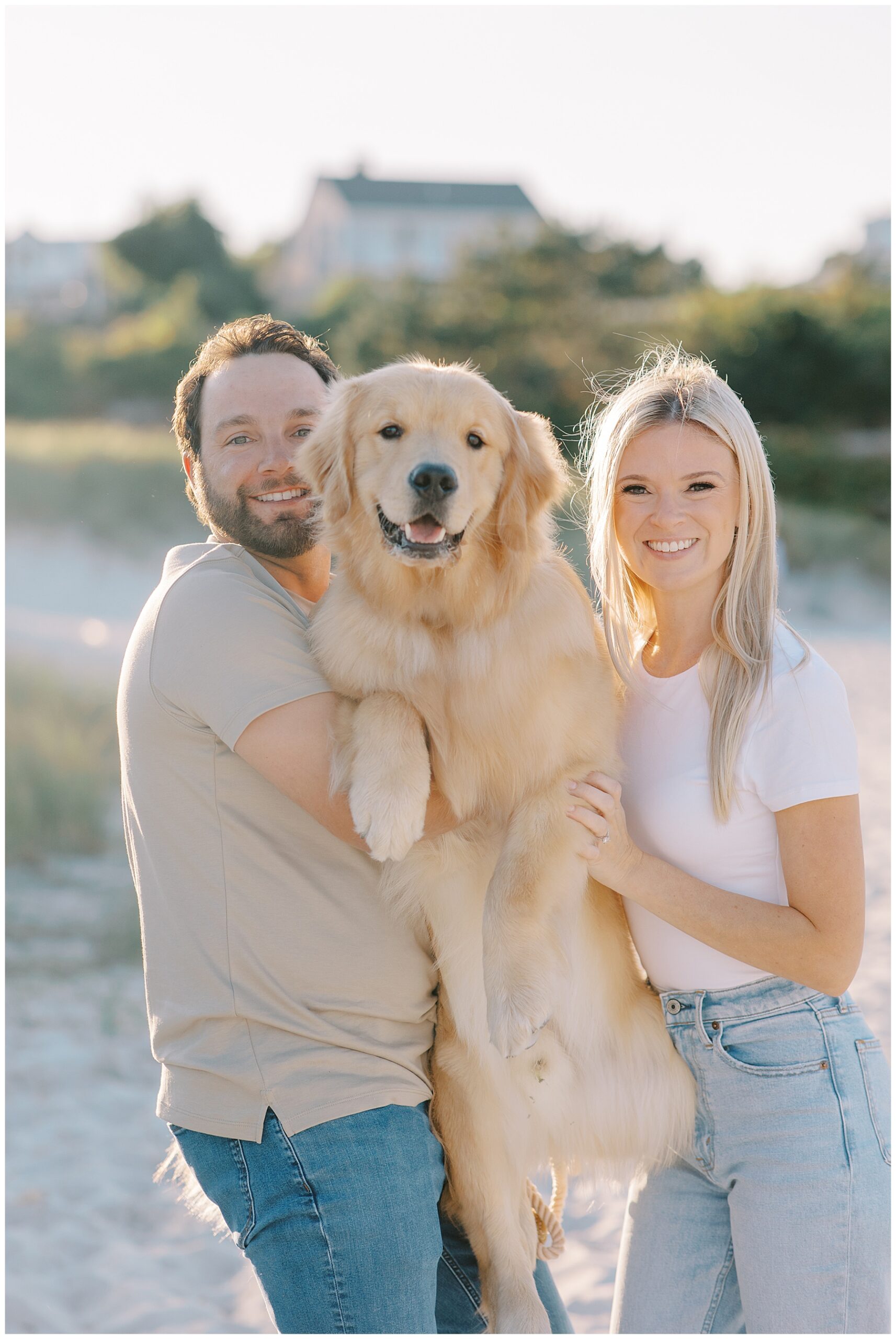 couple hold their golden retriever during relaxed beach engagement