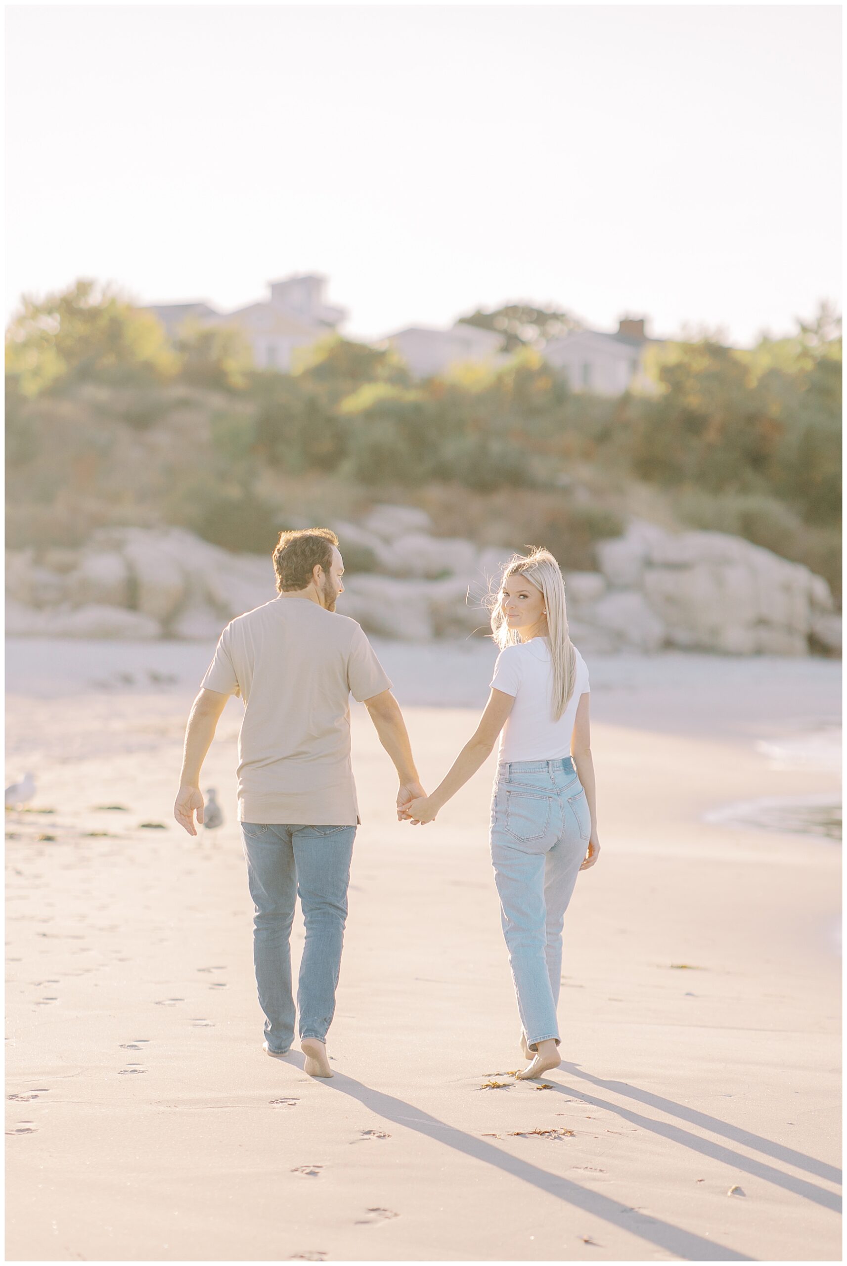 engaged couple hold hands as they walk along beach