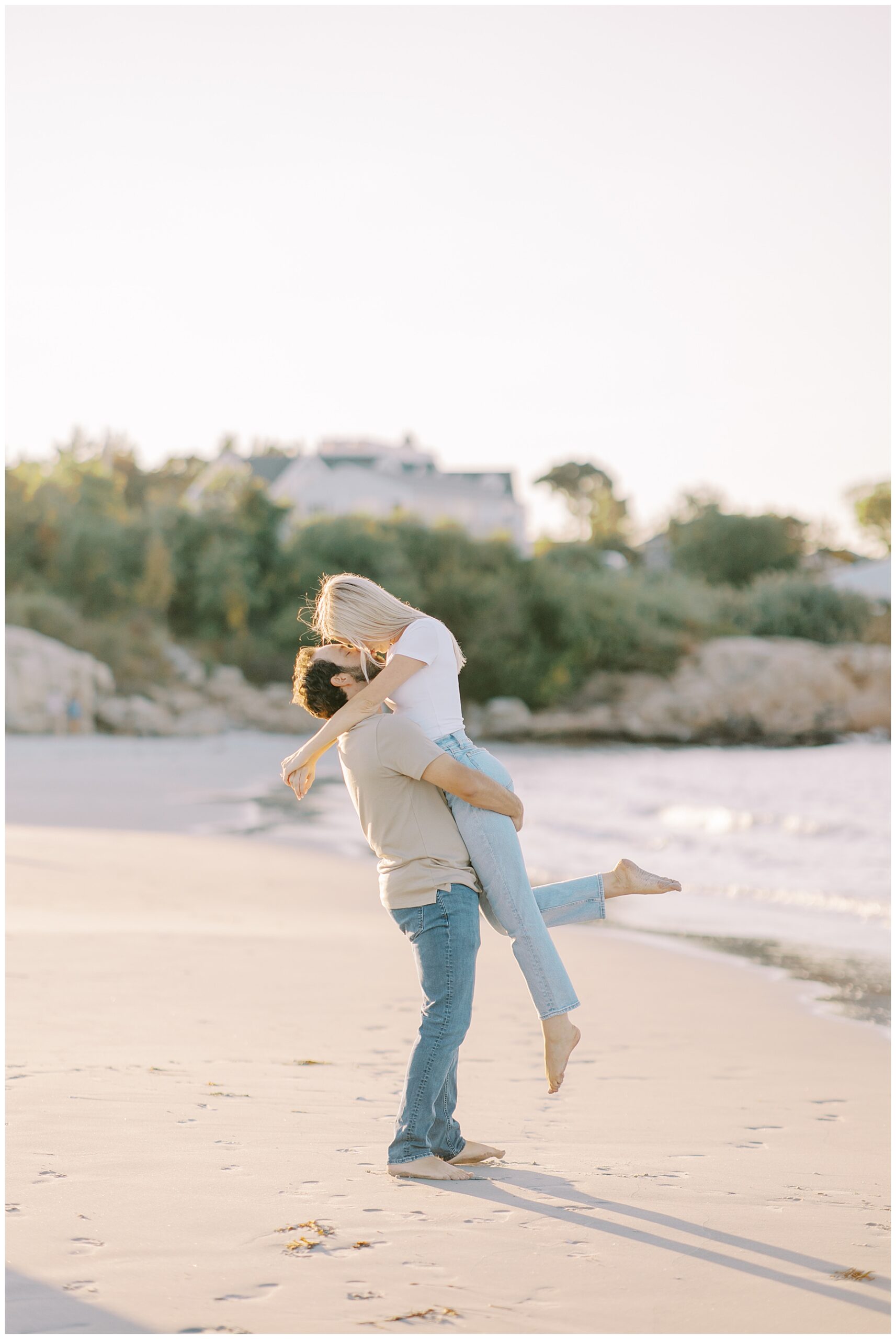man lifts up his fiance on the beach during engagement session