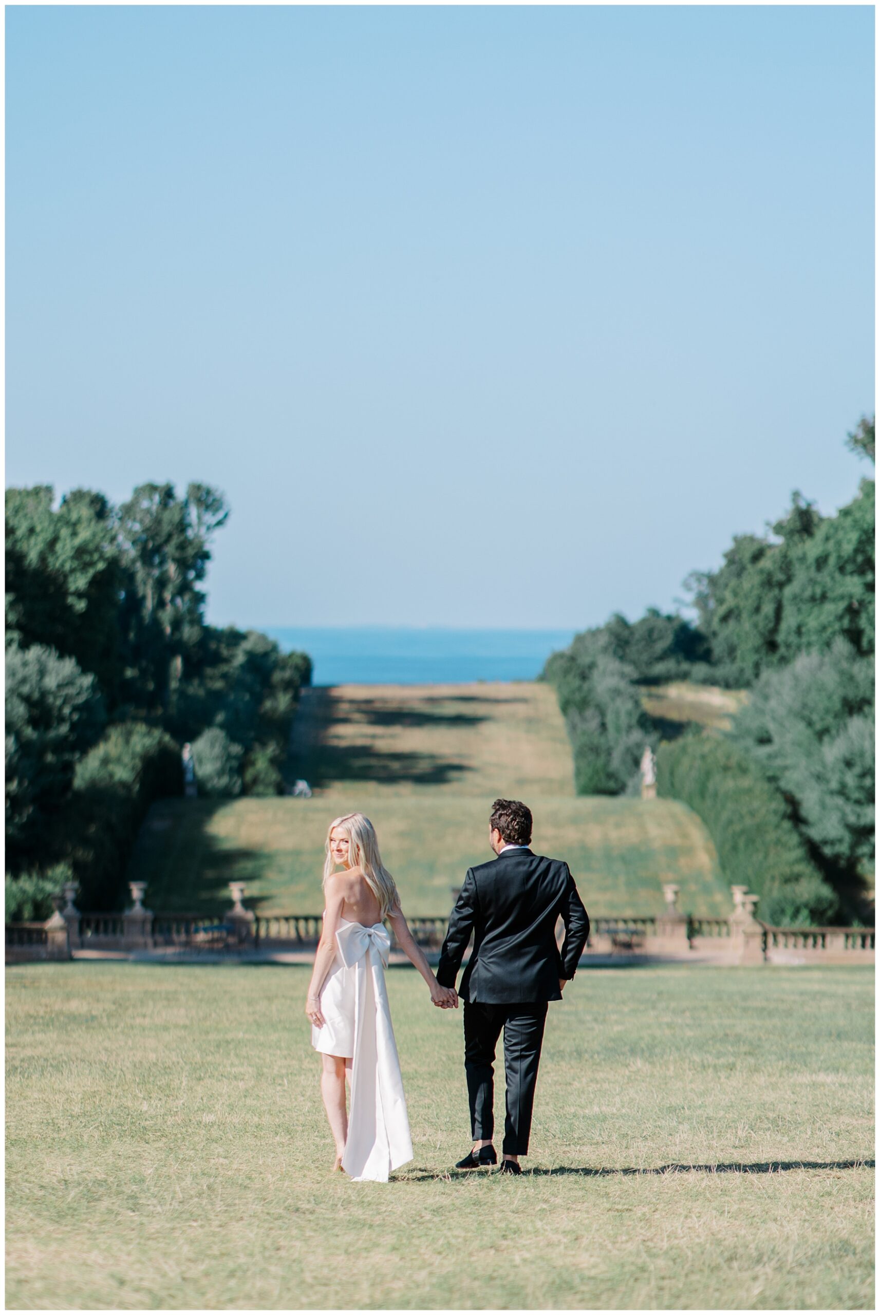 couple walk down lawn toward the ocean views in Ipswich, MA