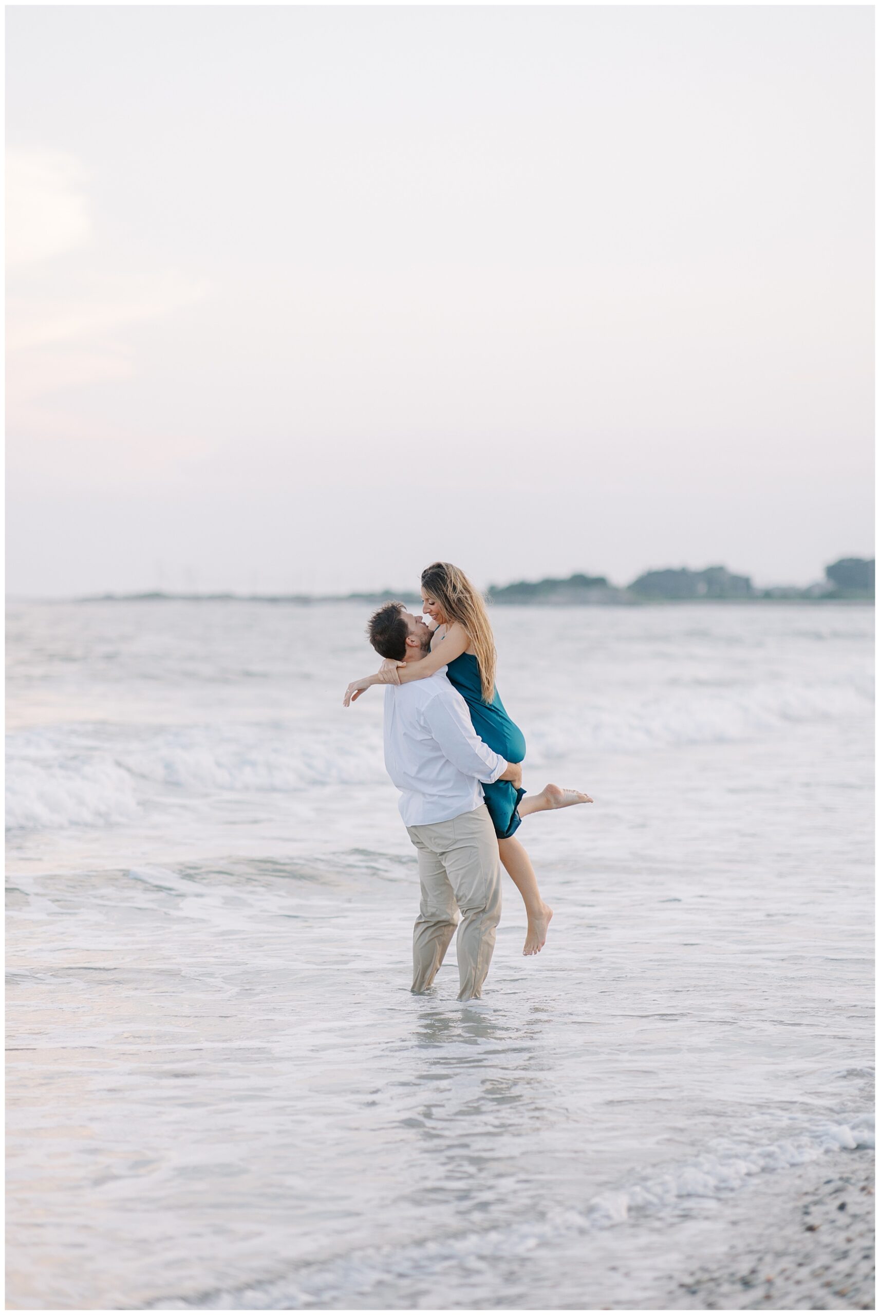 Romantic Westport MA Engagement photo of guy lifting woman up while standing in ocean