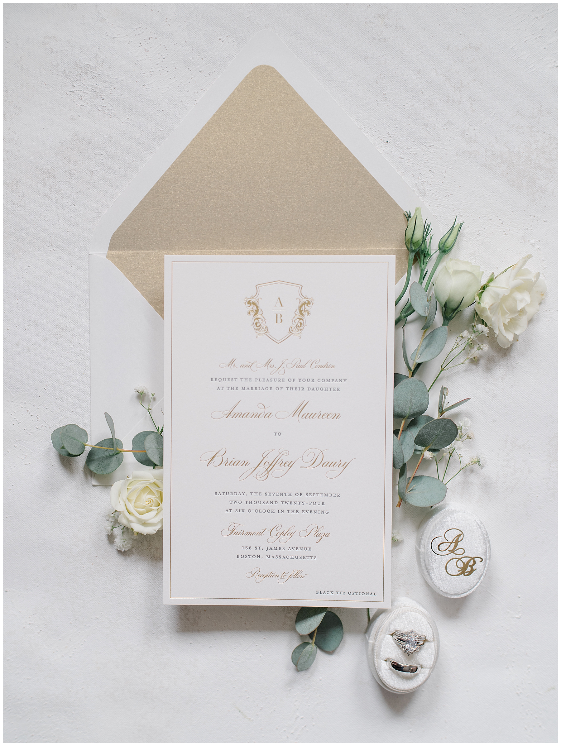 white and gold invitation suite surrounded by soft greenery and white background
