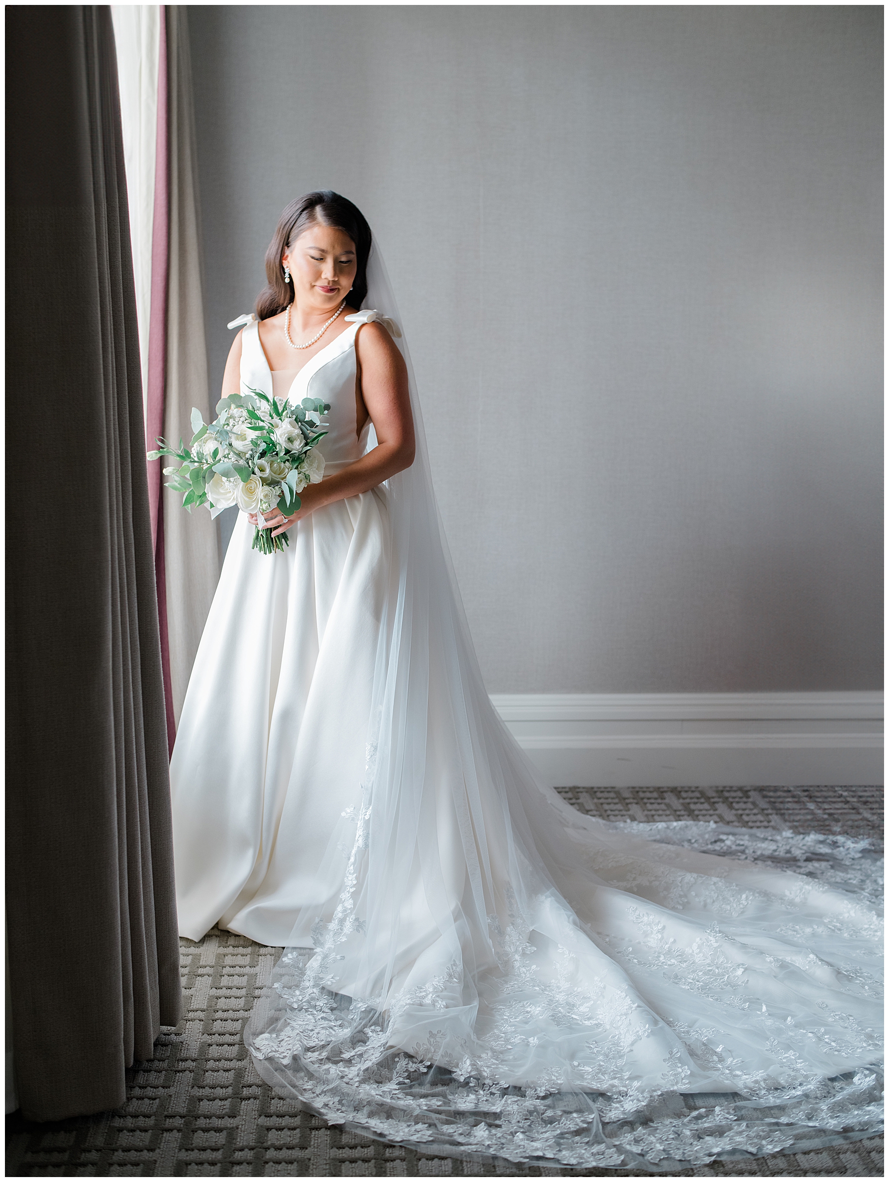 bride in wedding dress stands by window in hotel the morning of wedding