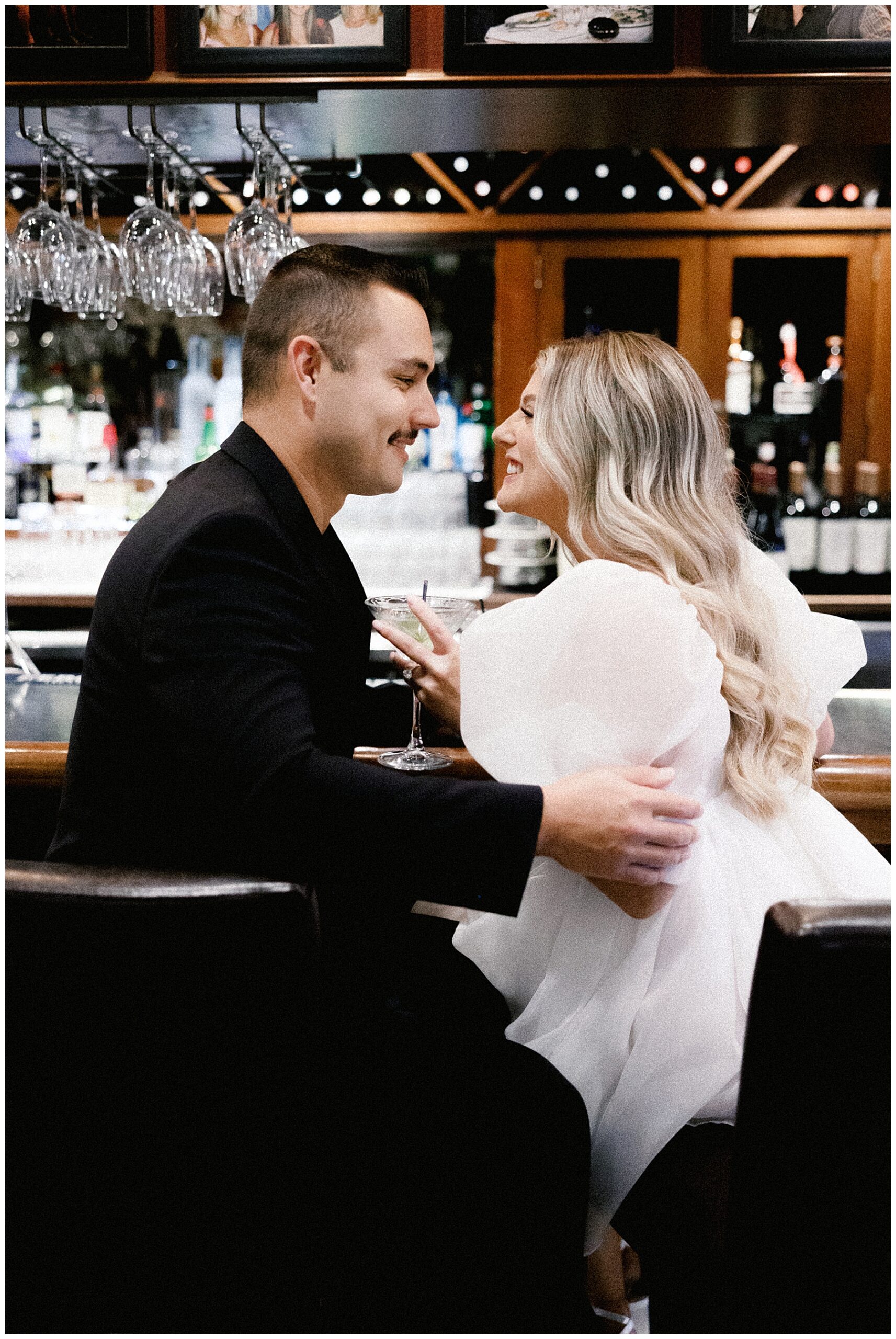 engaged couple sit together at bar and lean towards each other