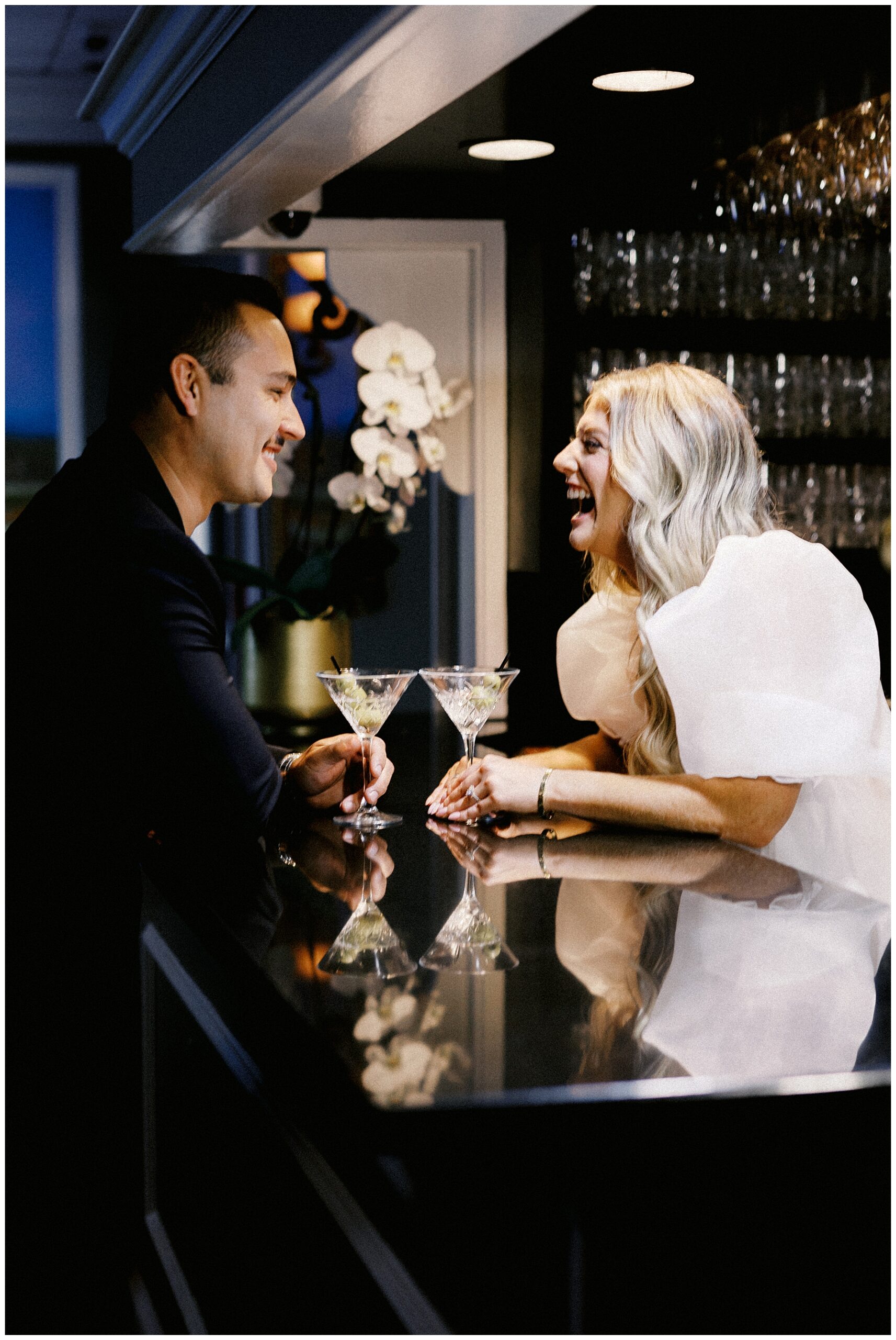 couple laugh as they sit across bar from each other