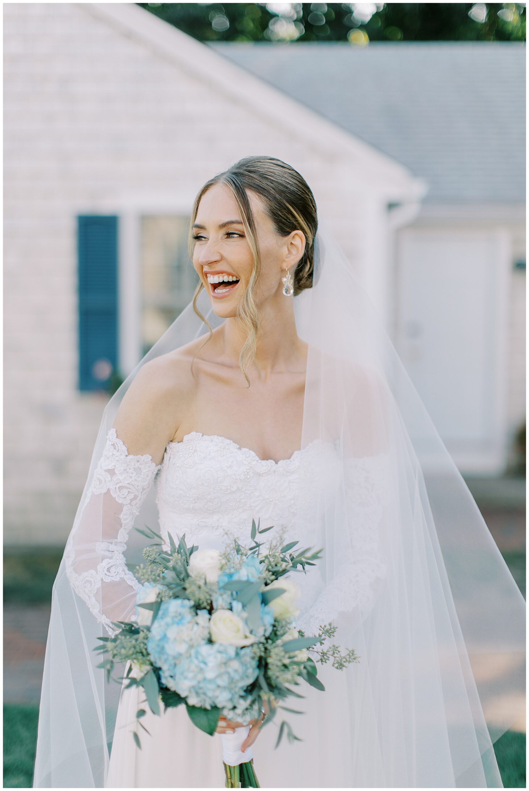 Bride laughs and looks off to the side while holding blue hydrangea and white flower bouquet