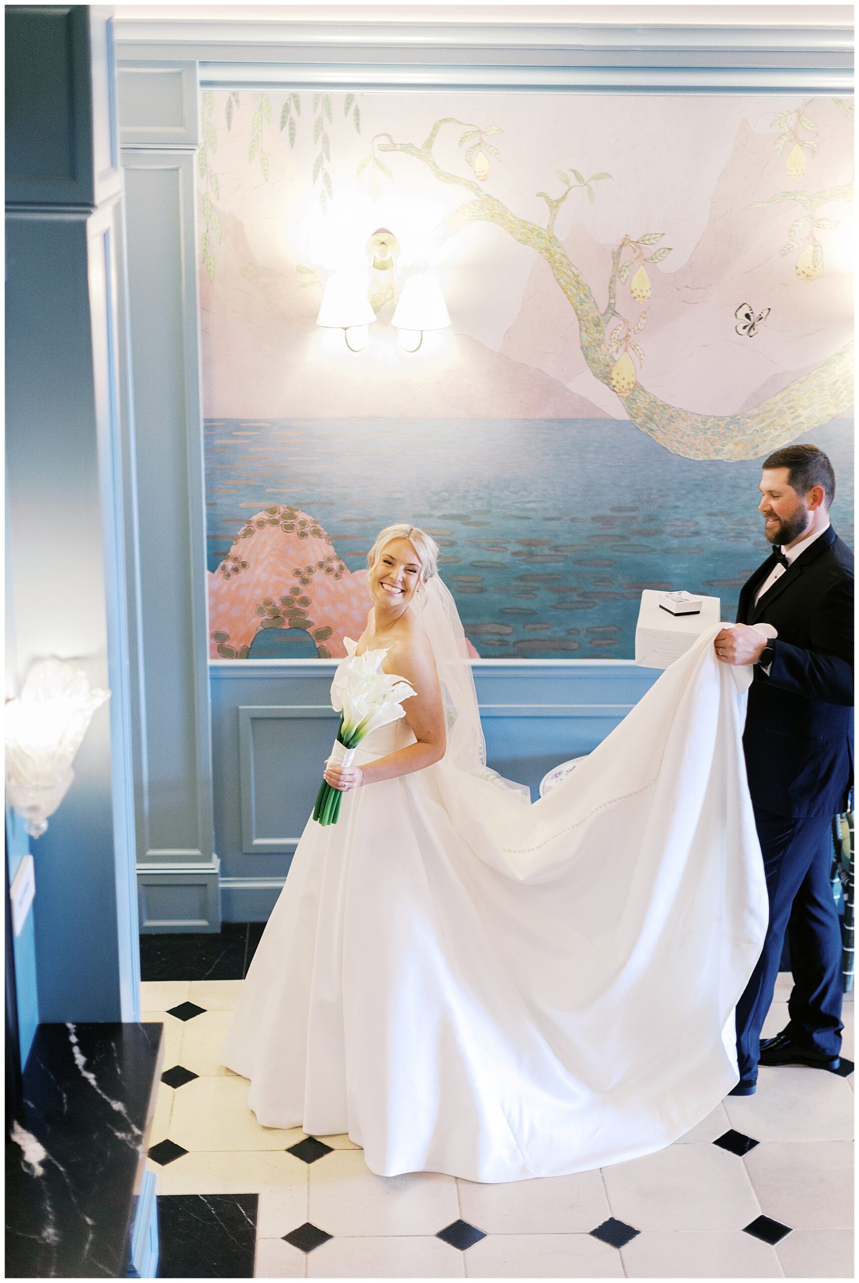 groom carries back of bride's wedding dress as they walk