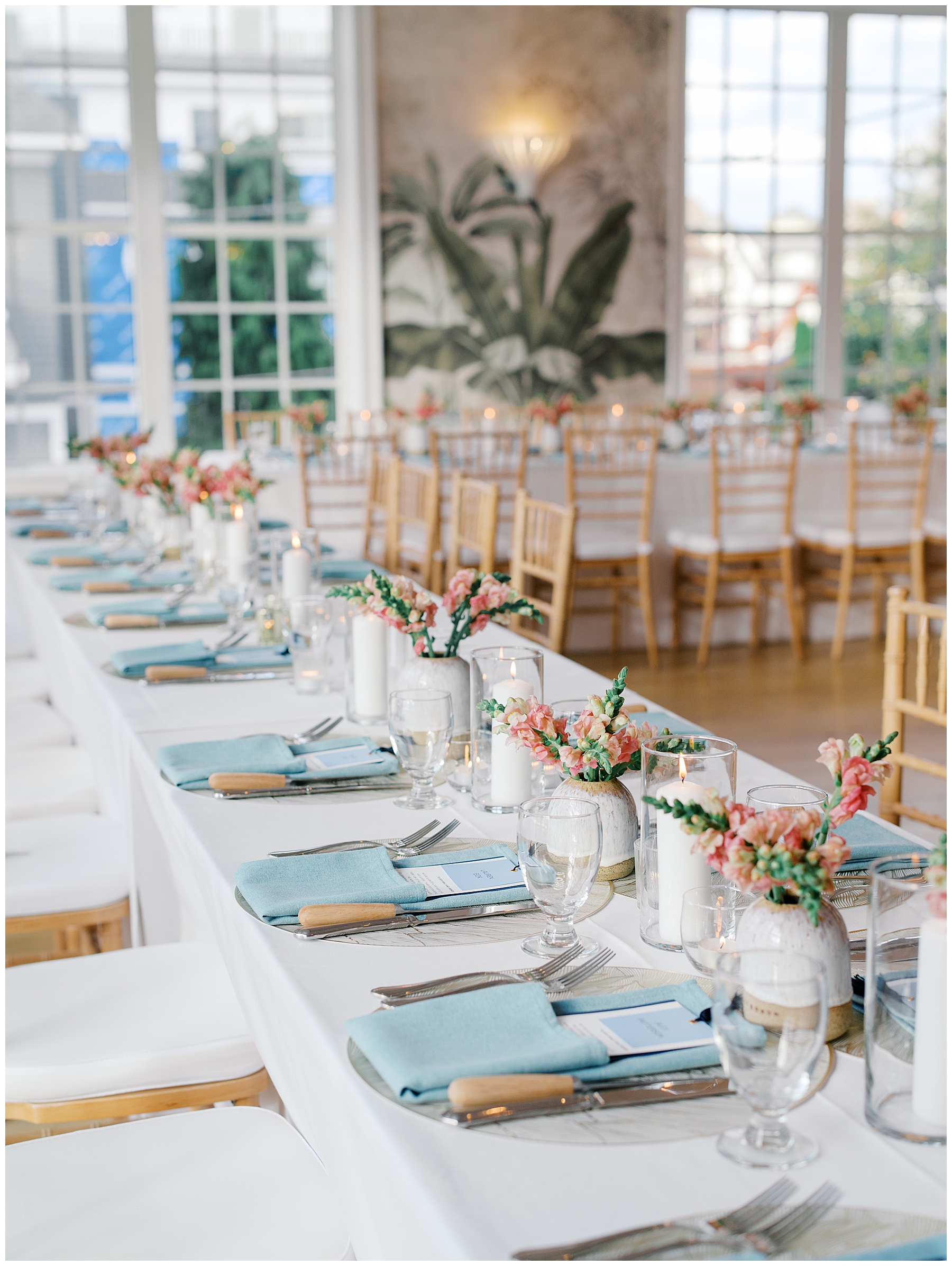 elegant tablescapes with menus tucked into blue napkins and vases hold light pink flowers and greenery