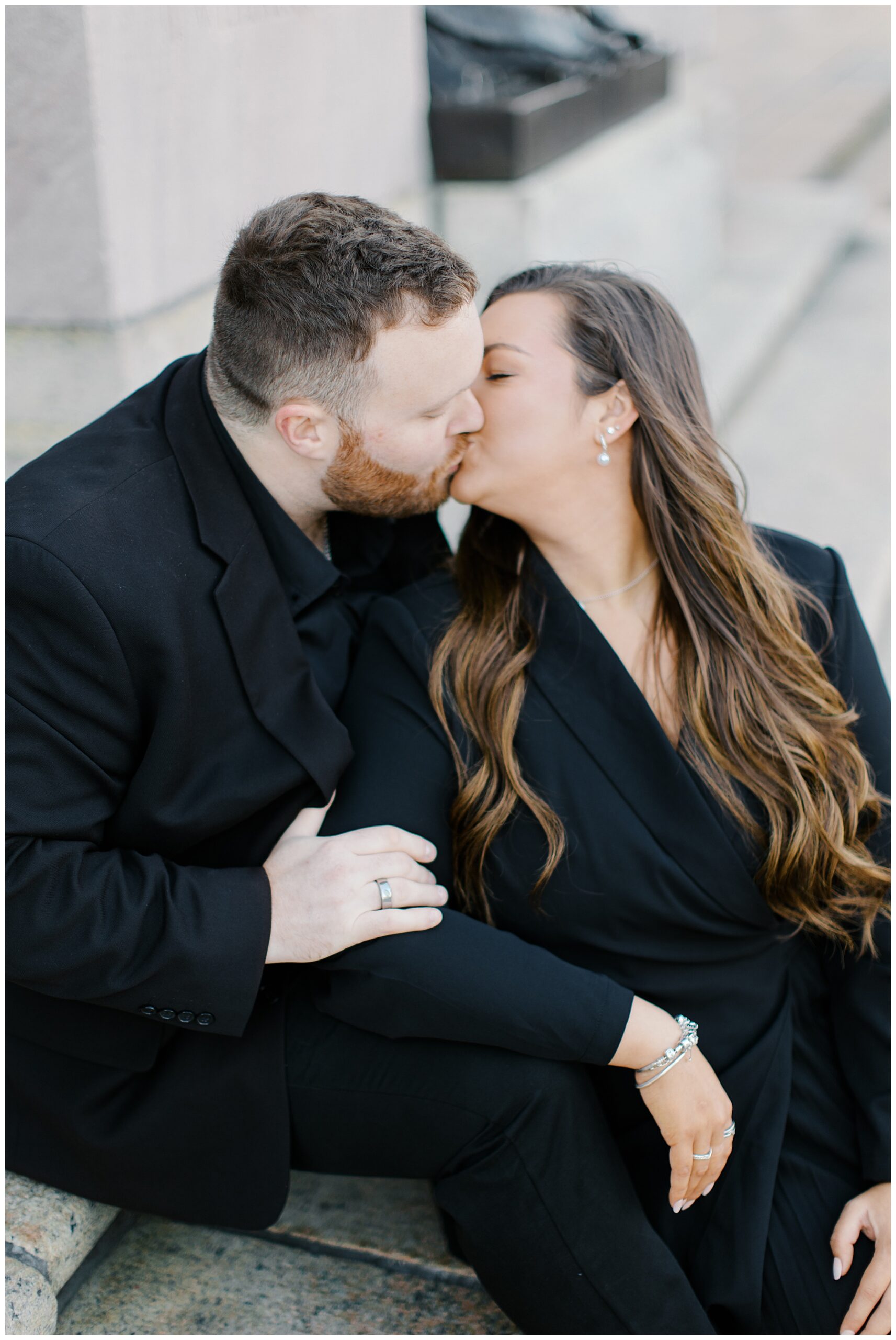 engaged couple kiss while sitting on steps of building 