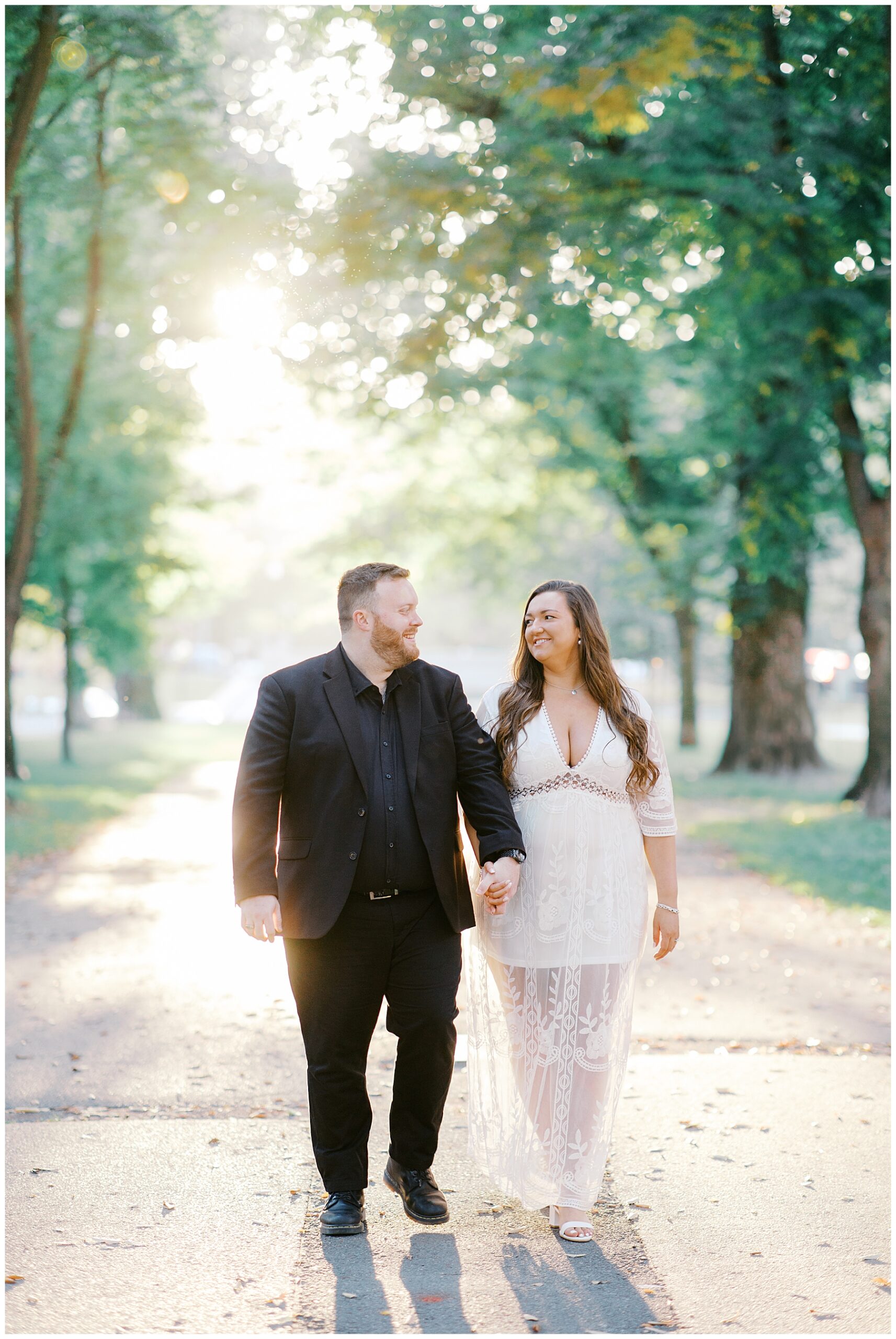 sunlight filters in through trees as couple walk together holding hands