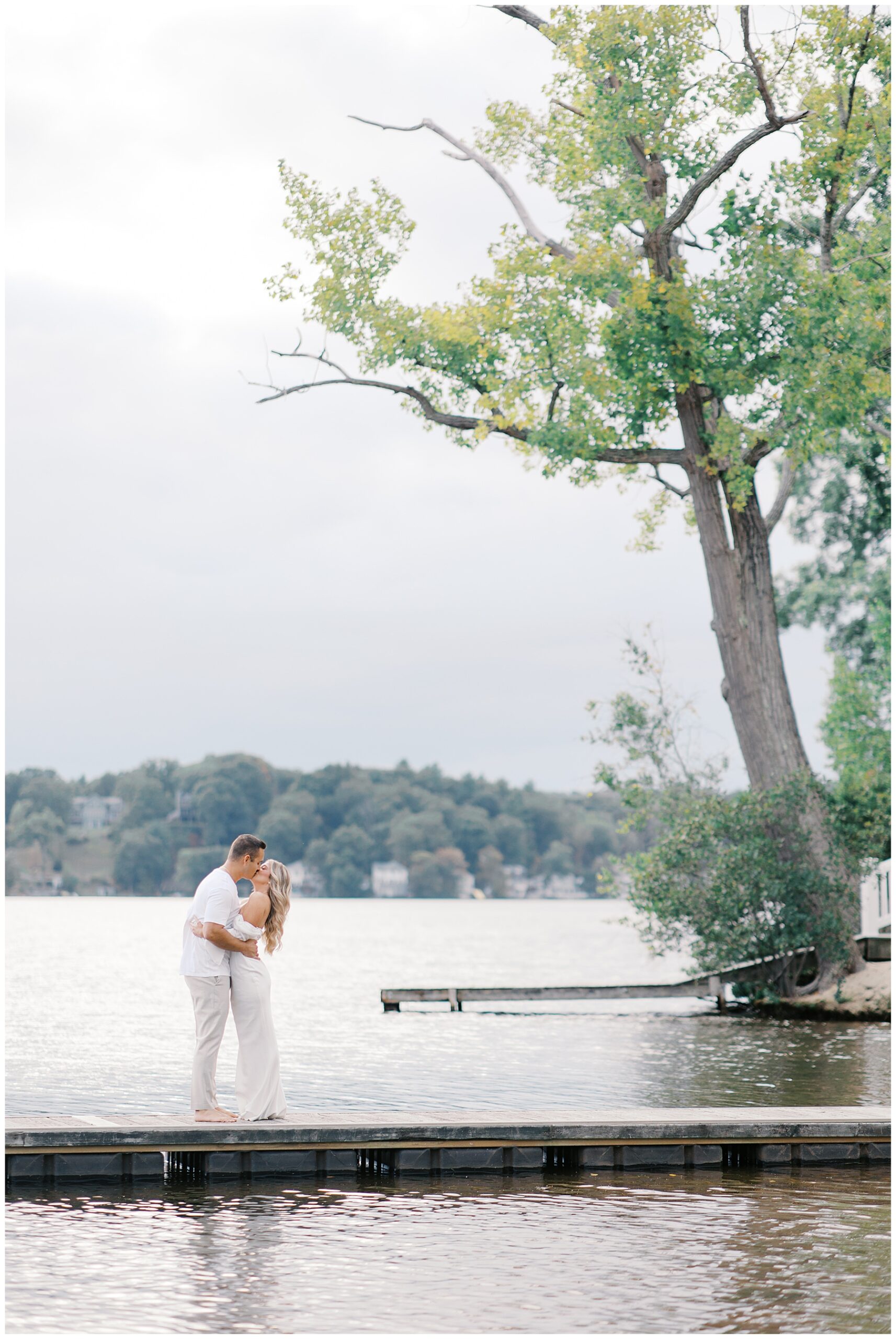 engaged couple kiss on dock on the water