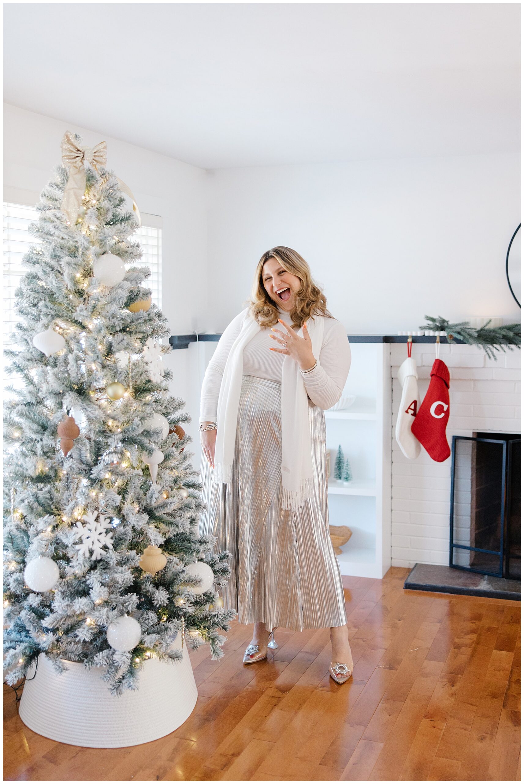 woman shows off engagement ring standing by elegantly decorated Christmas tree