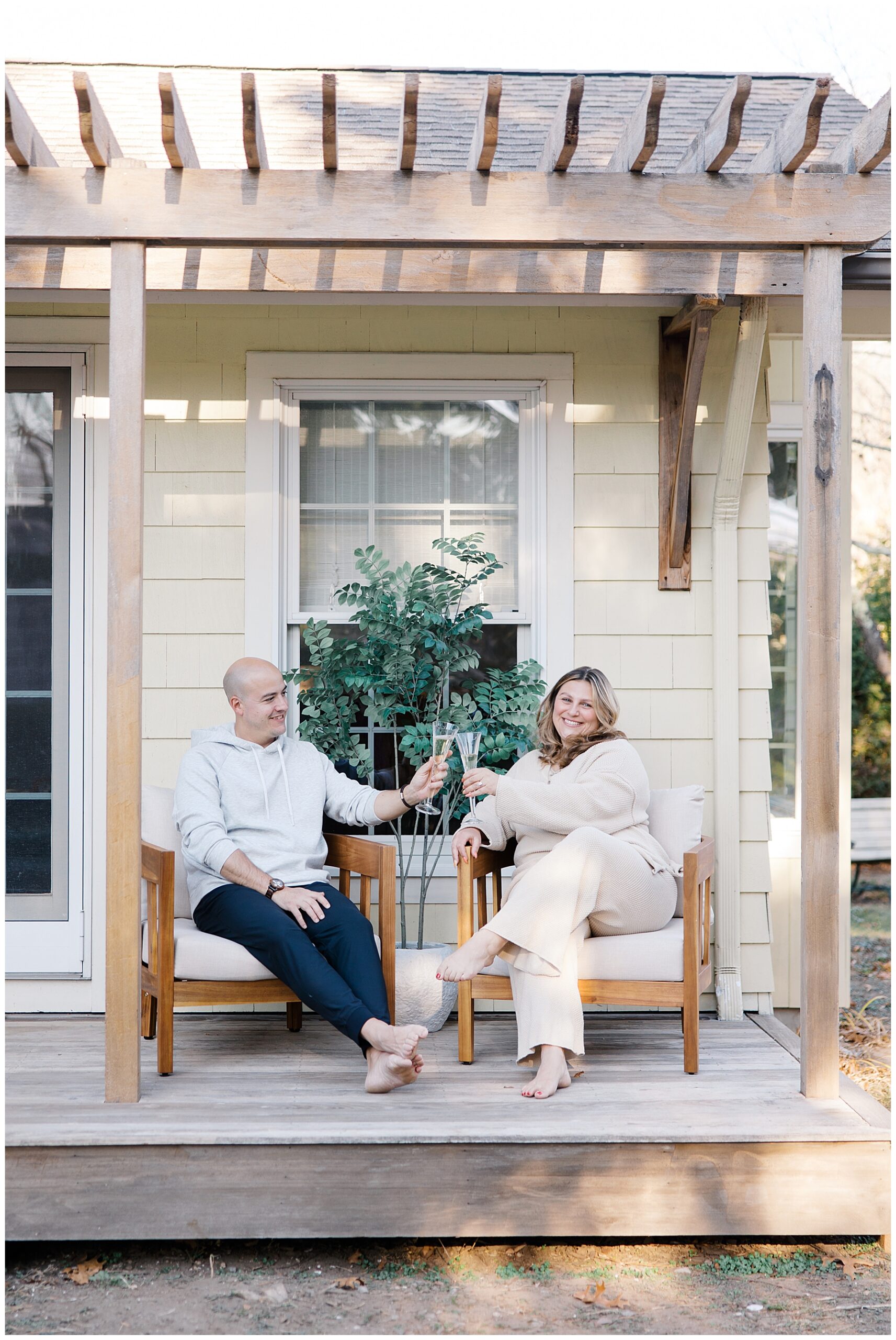 couple sit on back porch of home toasting with a glass of champagne after Surprise Christmas Proposal in Rhode Island 