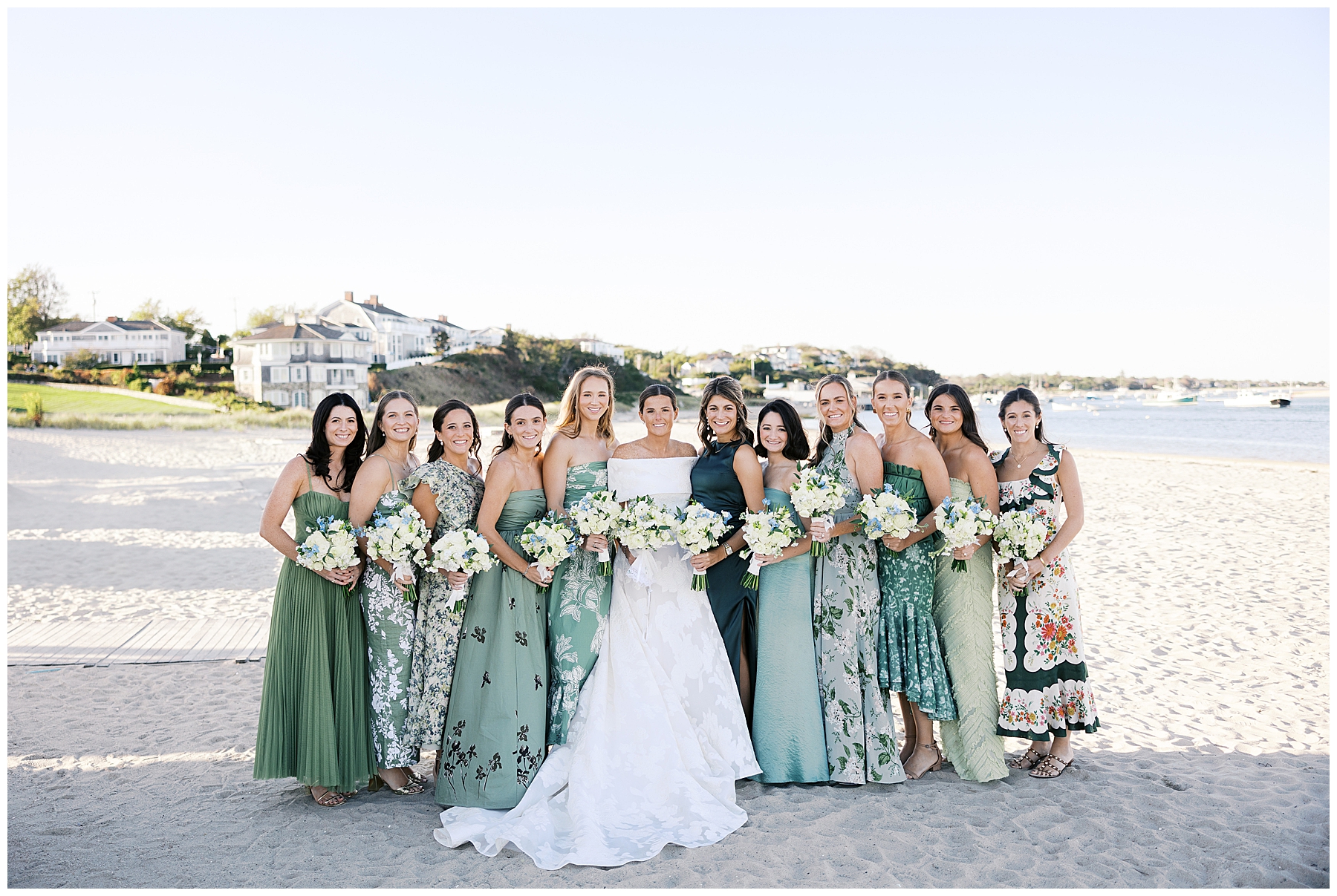 bridesmaids in different green bridesmaids' dresses surround bride on the beach 