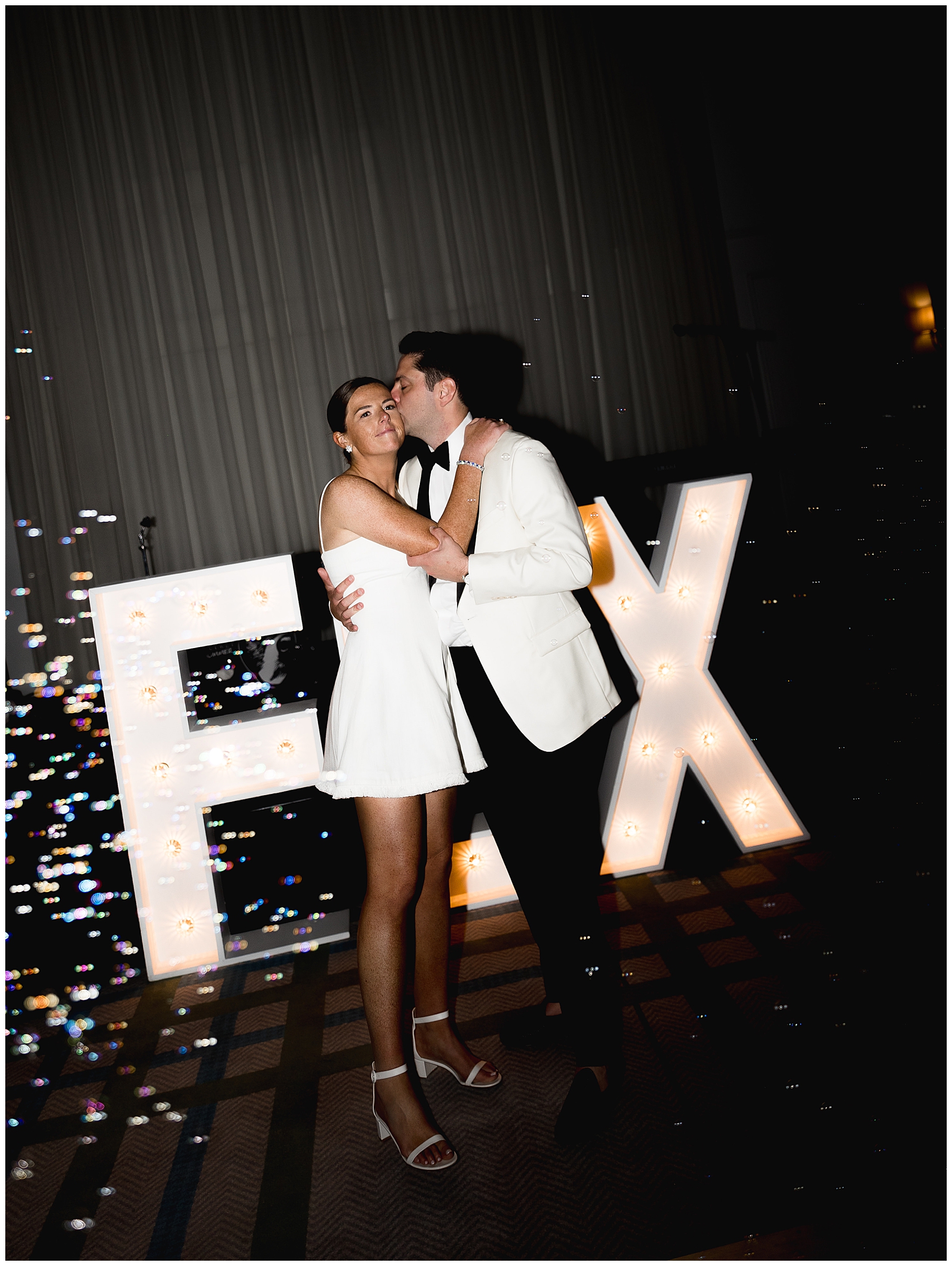 newlyweds in front of last name light up sign 