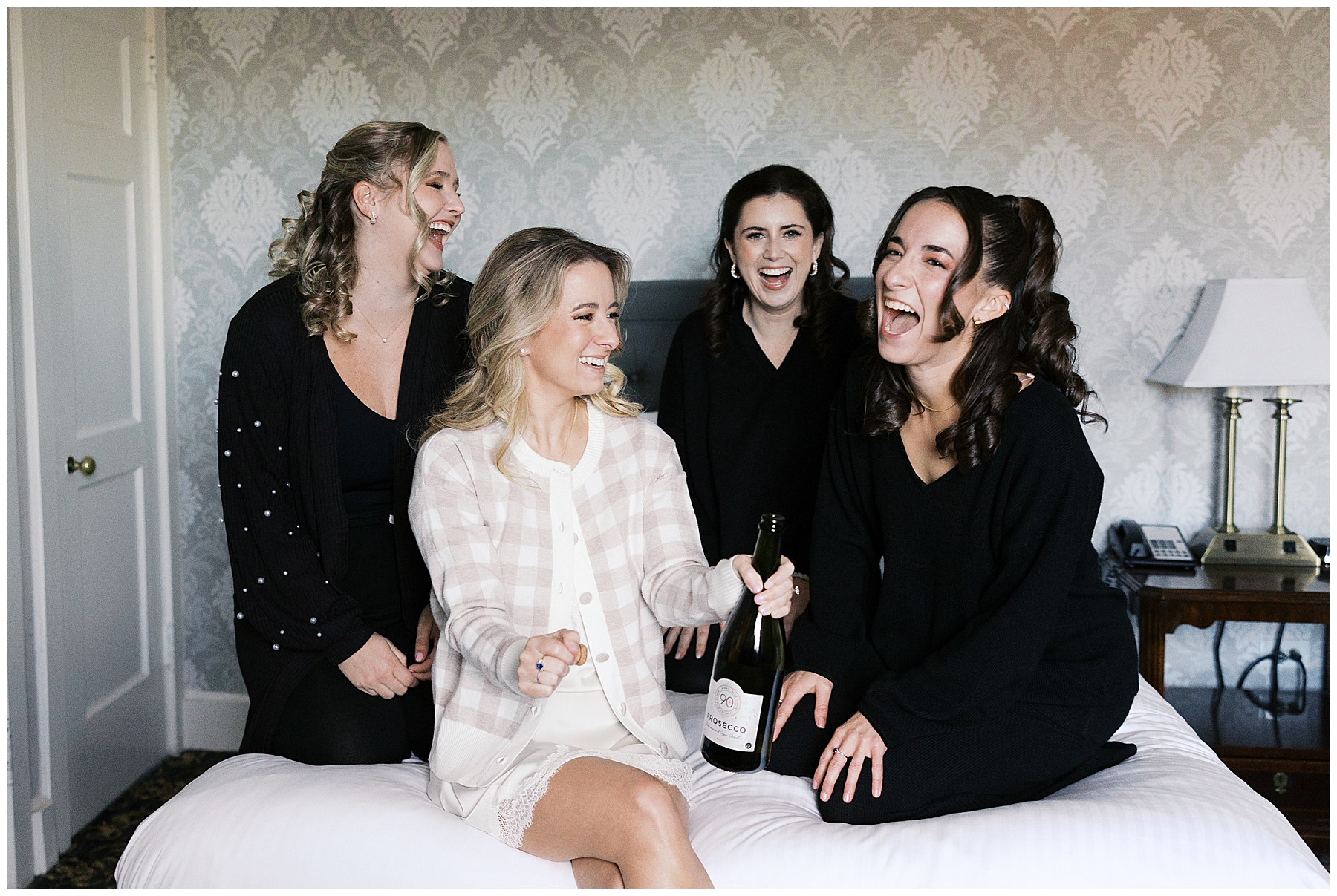 bride and bridesmaids on bed with champagne
