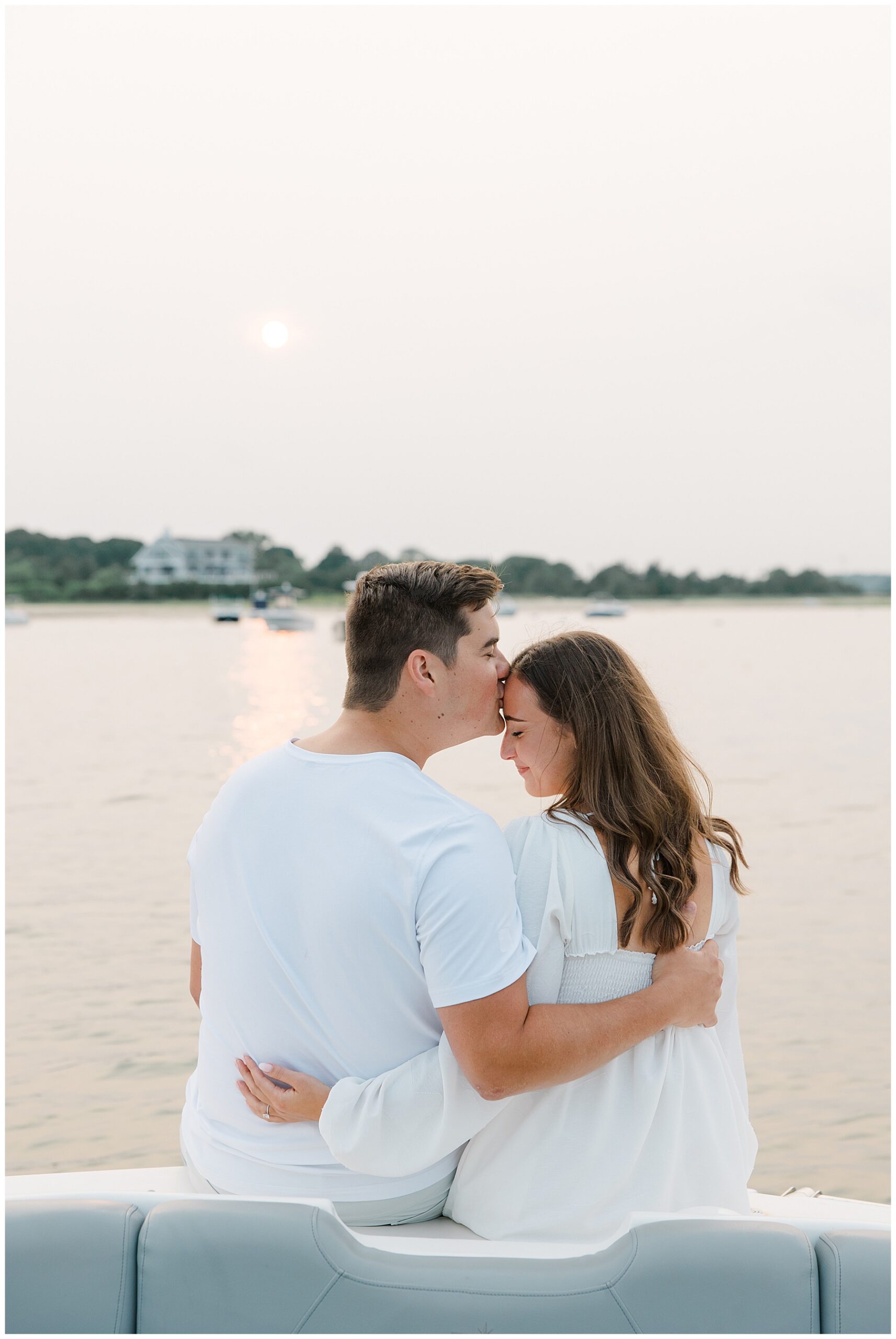 man kisses fiancé as they sit on back of boat