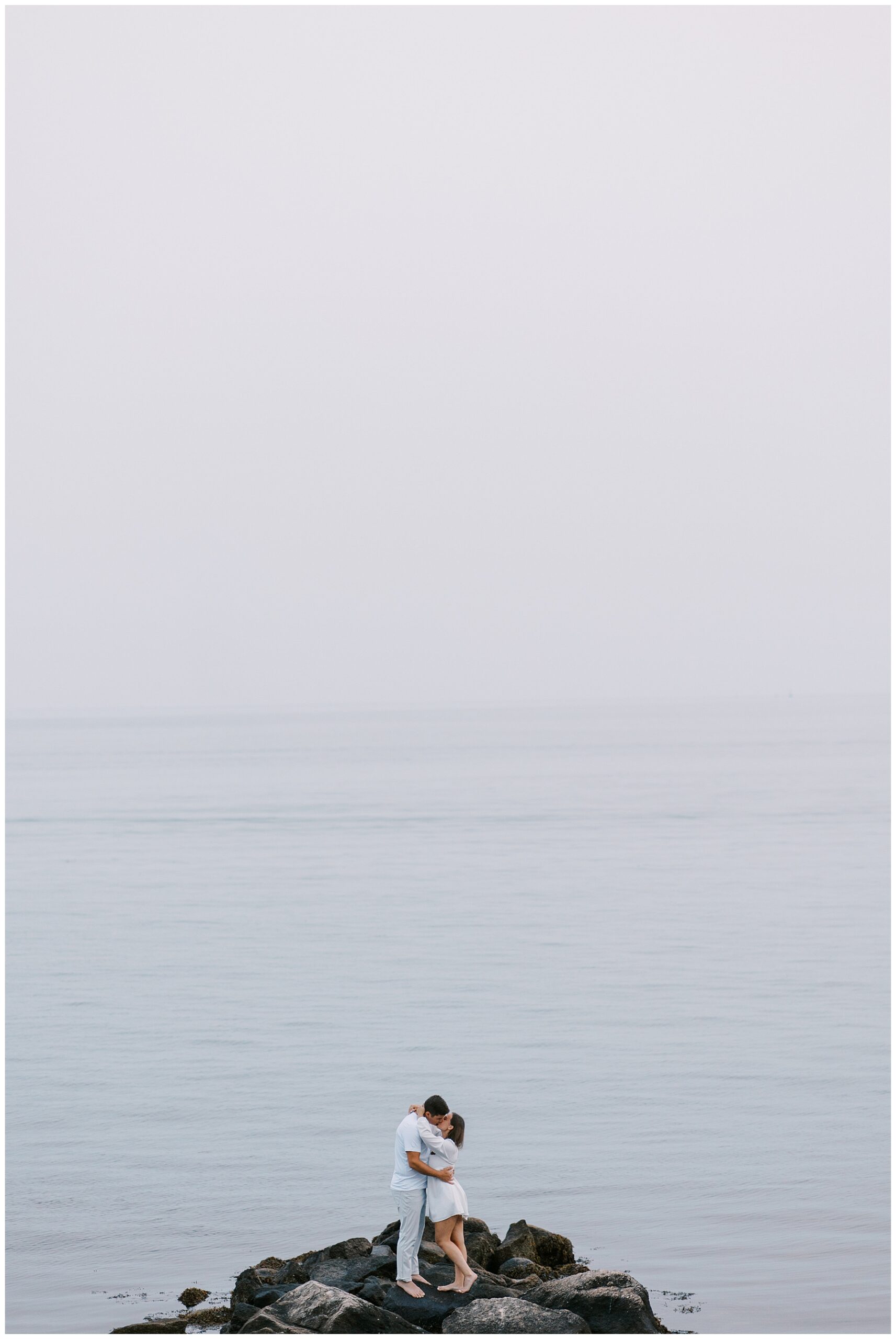 engaged couple kiss on rocky shore in Cape Cod