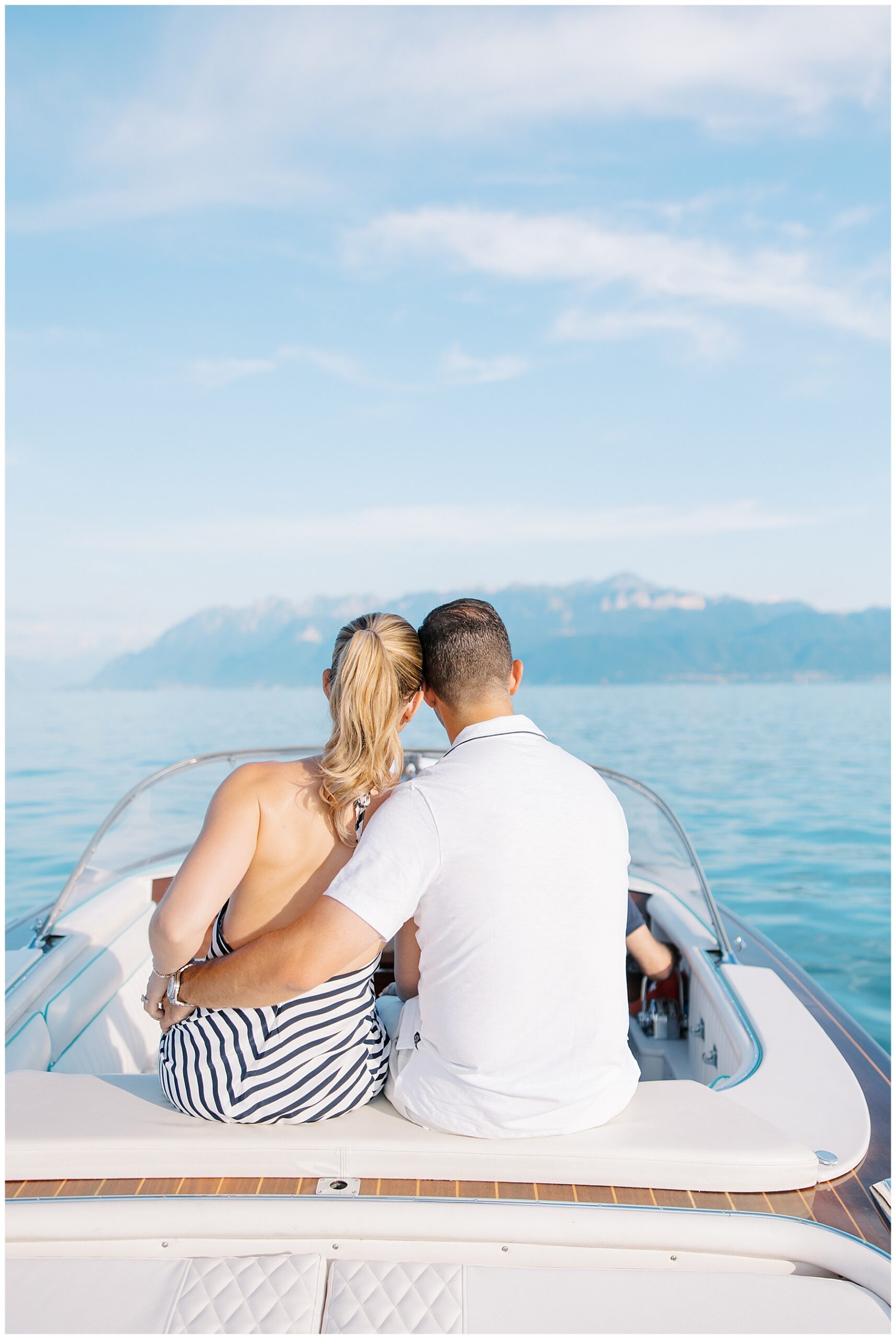 couple sit on back of boat and take in views of the Alps in the distance