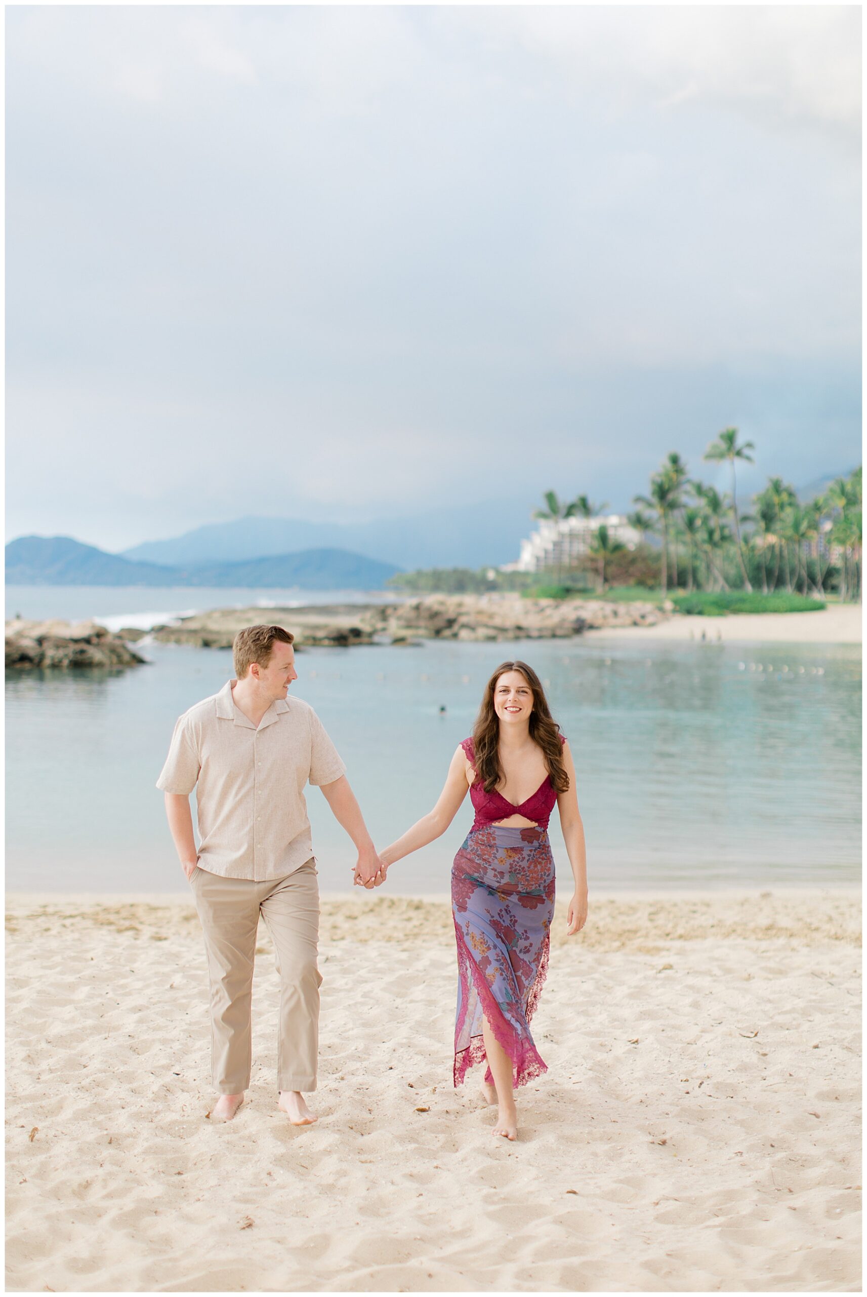 engaged couple hold hands as they walk the beach together in Hawaii