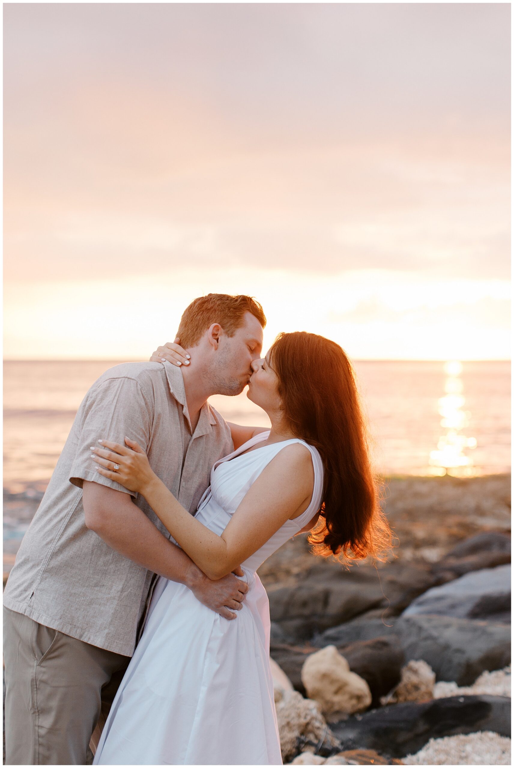 couple kiss by the ocean at sunset in O'ahu Hawaii