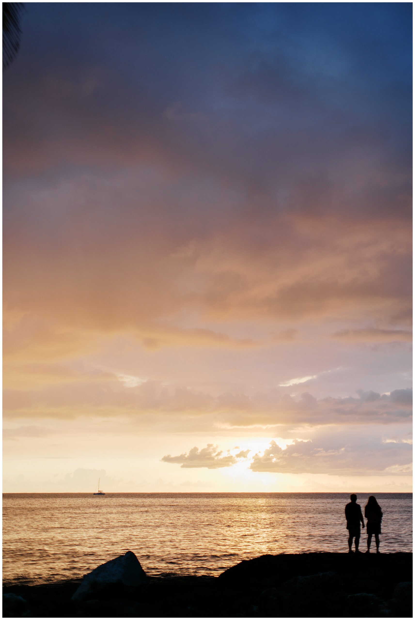 couple stand on rocks and enjoy the sunset over the ocean in O'ahu Hawaii