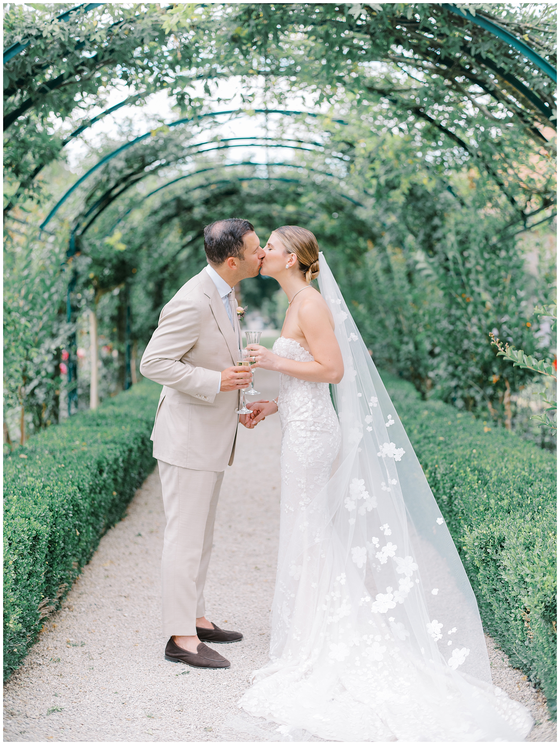 bride and groom kiss in garden walkway with champagne